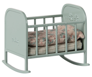 A blue mint colored metal cradle with a soft sleeping bag inside, featuring small flower embossment on the headboard and rounded legs.