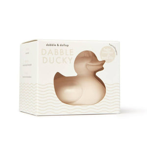 A beige rubber ducky bath toy in its packaging, labeled 'Dabble & Dollop' and noted as latex-free.