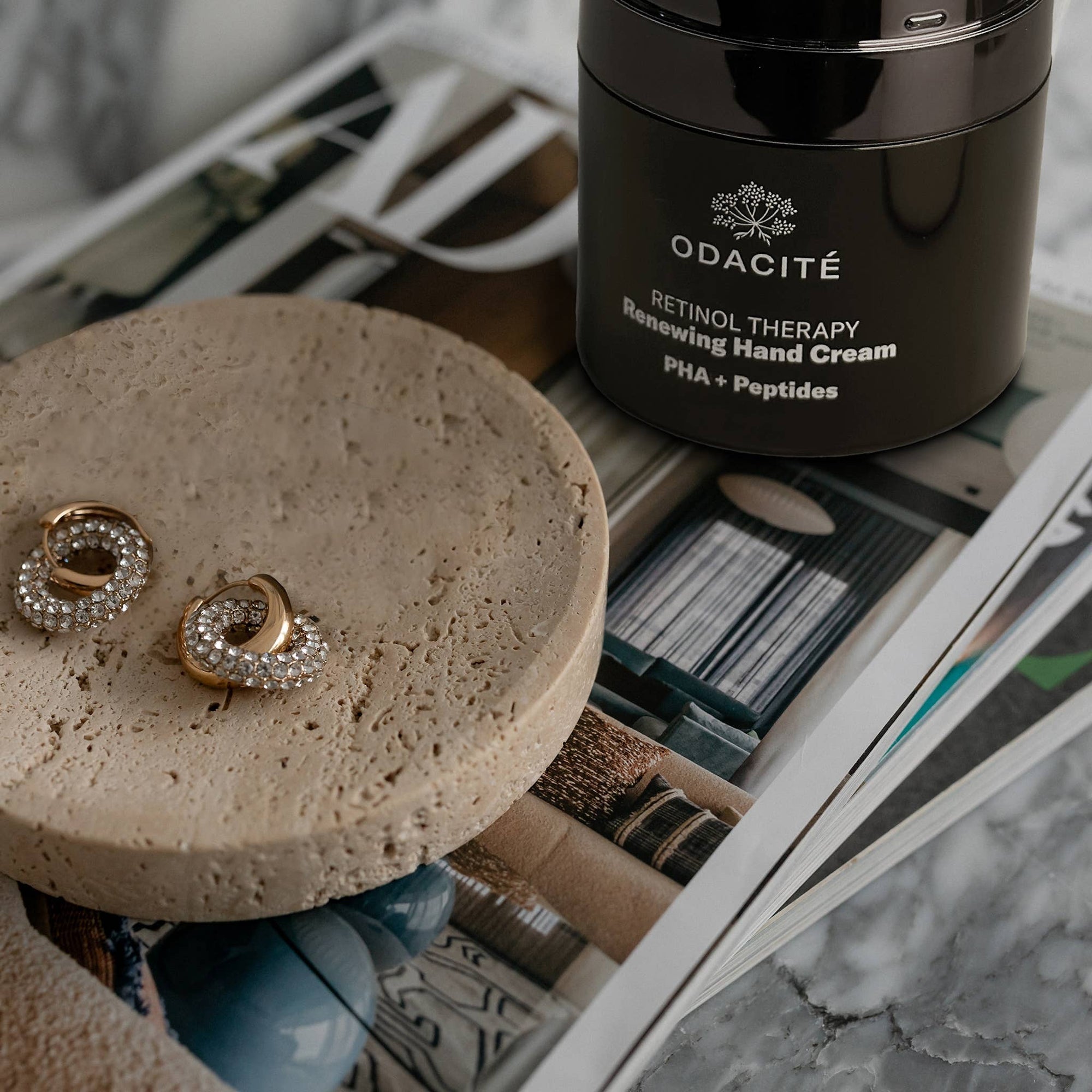 Odacite retinol therapy hand cream jar with earrings on a round stone surface