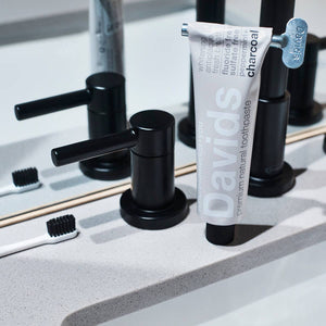 A tube of David's charcoal toothpaste in front of a sink.