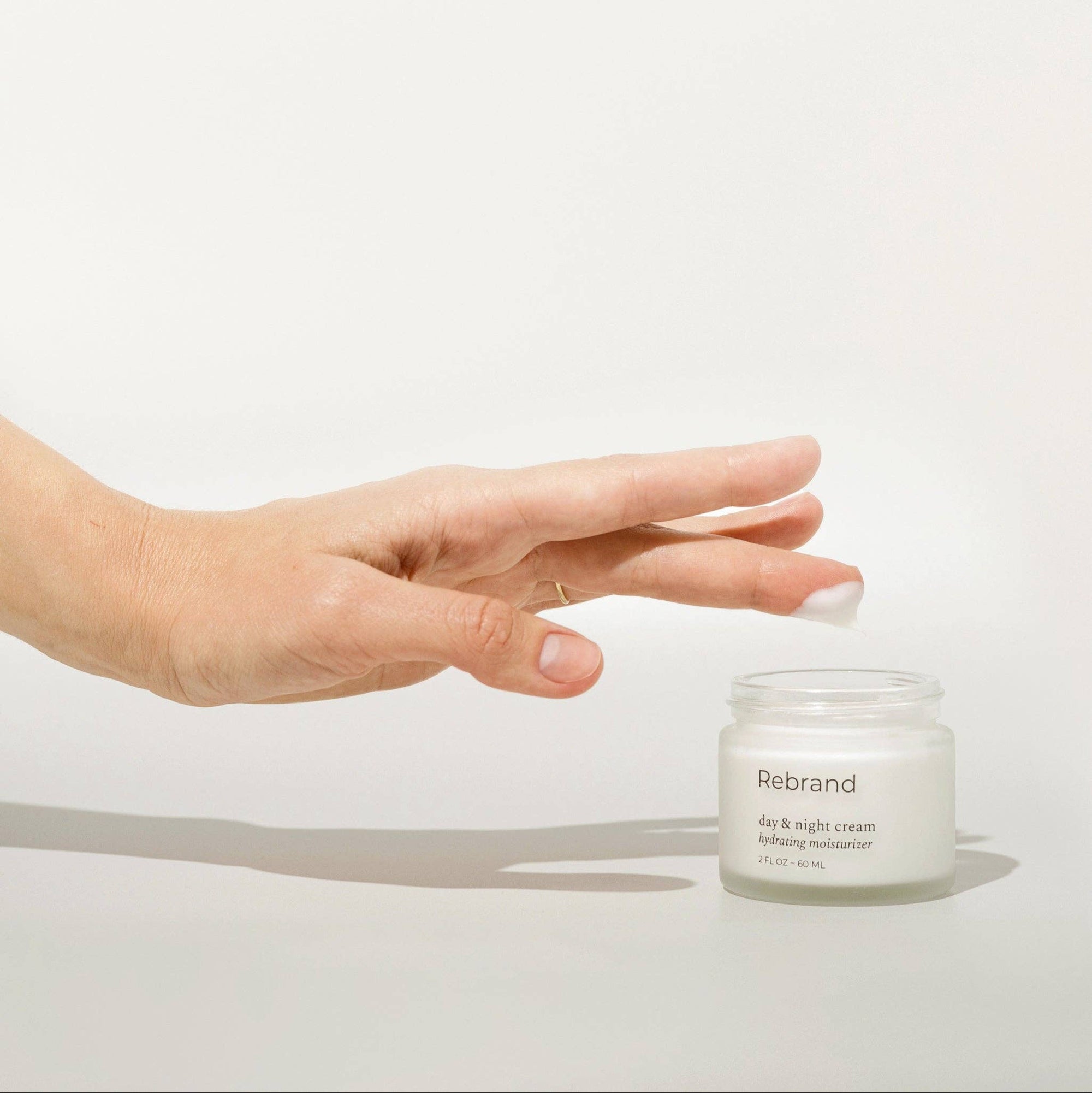 Hand holding a jar of Rebrand eye and night cream on a white background