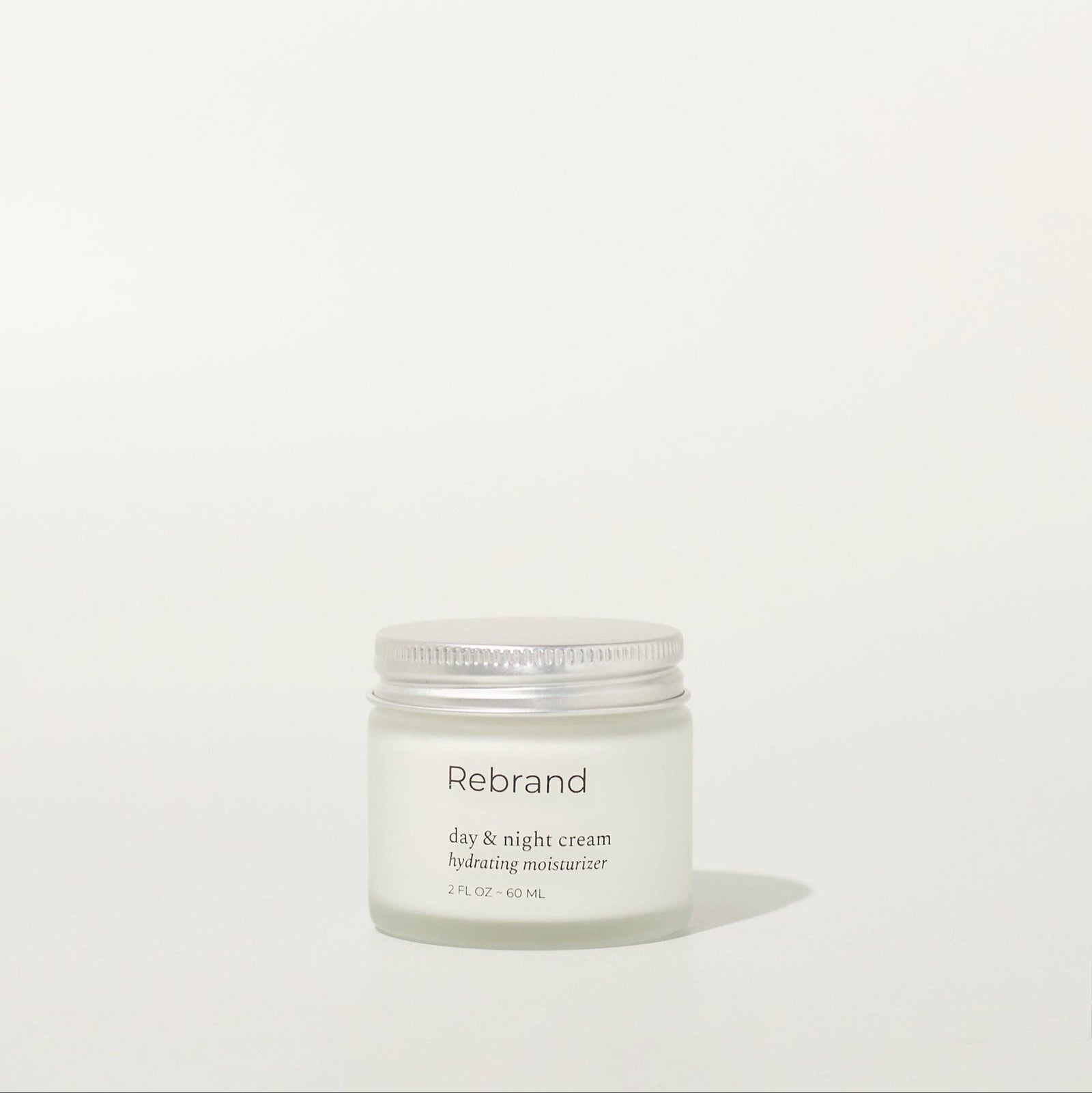 Hand holding a jar of Rebrand eye and night cream on a white background