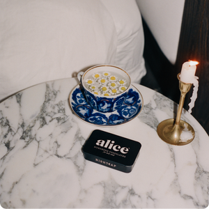 Teacup with saucer, candle, and 'alice' product on a marble surface