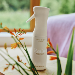White spray bottle labeled 'Realm' on a surface with plants in the foreground