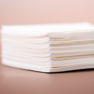 A stack of white kind laundry detergent sheets on a brown surface. 