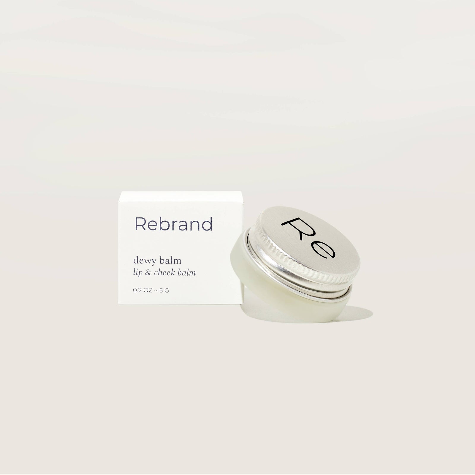 Silver jar of balm with 'Re' branding on a light beige background