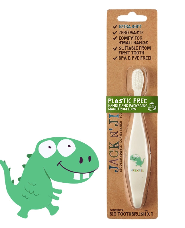 Packaging of Jack n' Jill Kids Dinosaur Toothbrush with a cartoon dinosaur design and product information, highlighting the toothbrush handle made from corn starch, suitable for first teeth, with extra soft bristles, BPA and PVC free, and supporting 1% for the Planet.