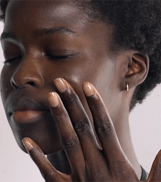 A bottle of Westman Atelier Vital Skincare Complexion Drops with a few drops spilled out on a white surface, showing the product color and consistency.