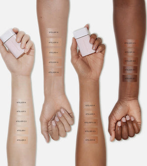 Hands holding complexion drops with color swatches on different skin tones.