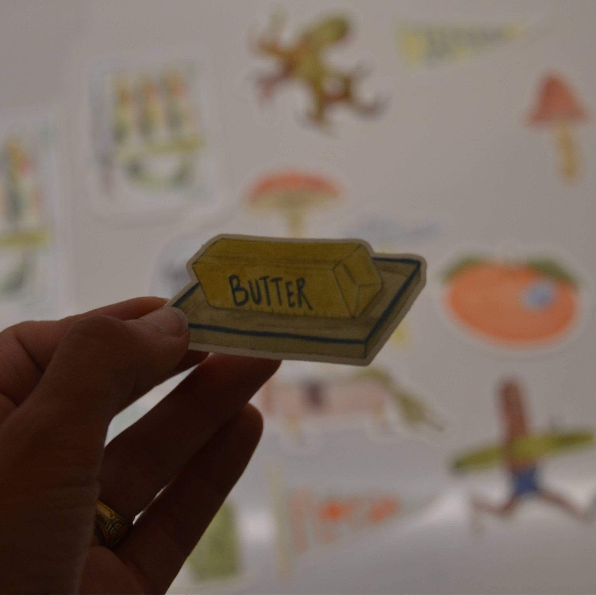Hand holding a card labeled 'Butter' with colorful illustrations in the background