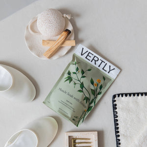 Bath products including a bath bomb, soap, and a magazine titled 'VERTLY' on a light surface.