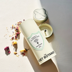 A cream colored tin labeled Edible Flower Mix, with flowers scattered around. 