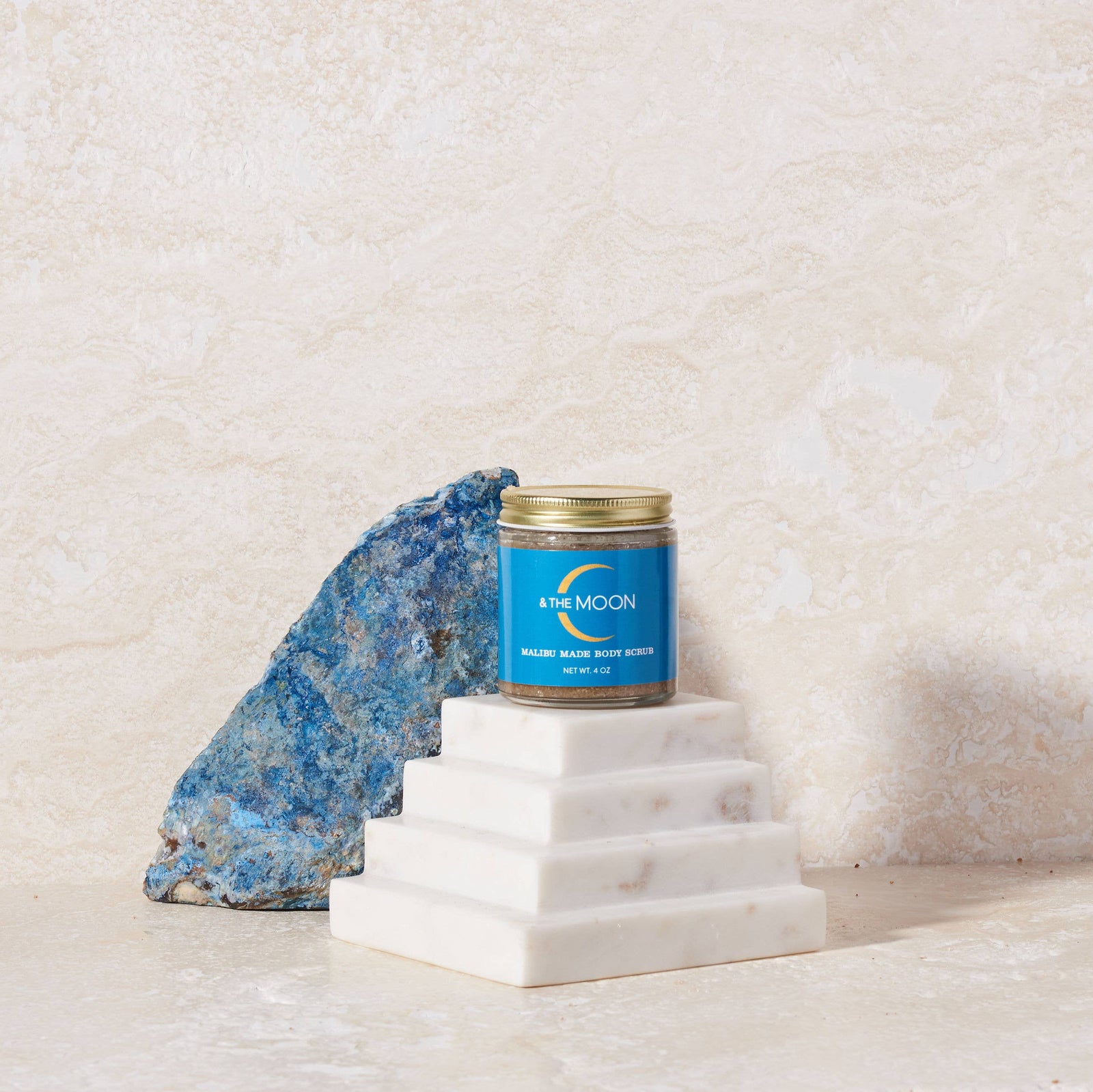 Jar of body scrub with blue label and gold lid on a light background