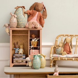 Collection of plush toys on a wooden shelf and chair against a light-colored wall.