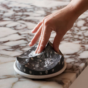 A hand touching an erode architectural soap on a marble counter. 