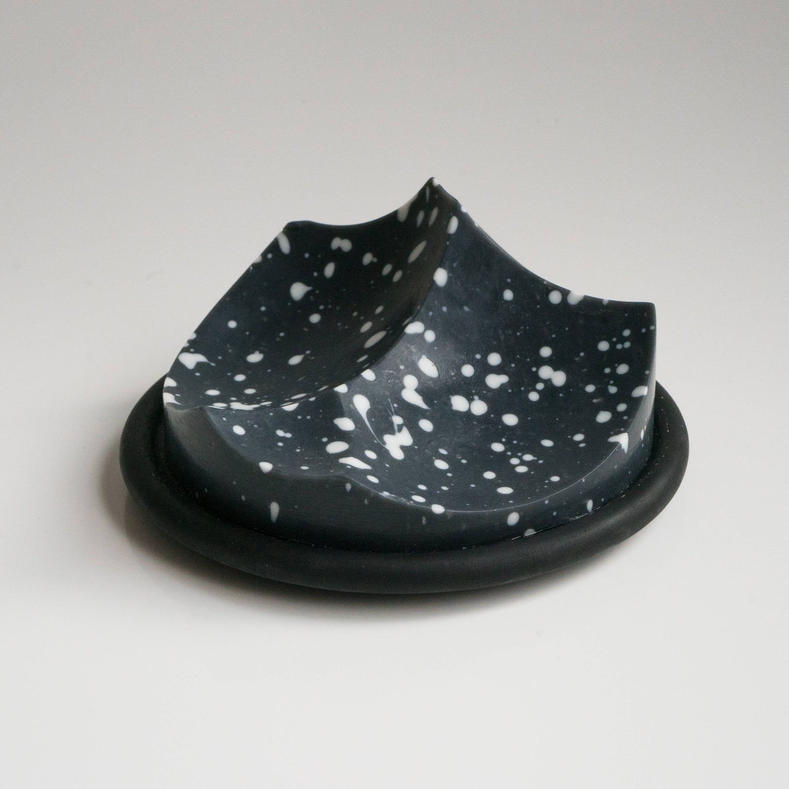 A uniquely shaped bar of soap with a black base and speckled with white dots, resting on a black surface.