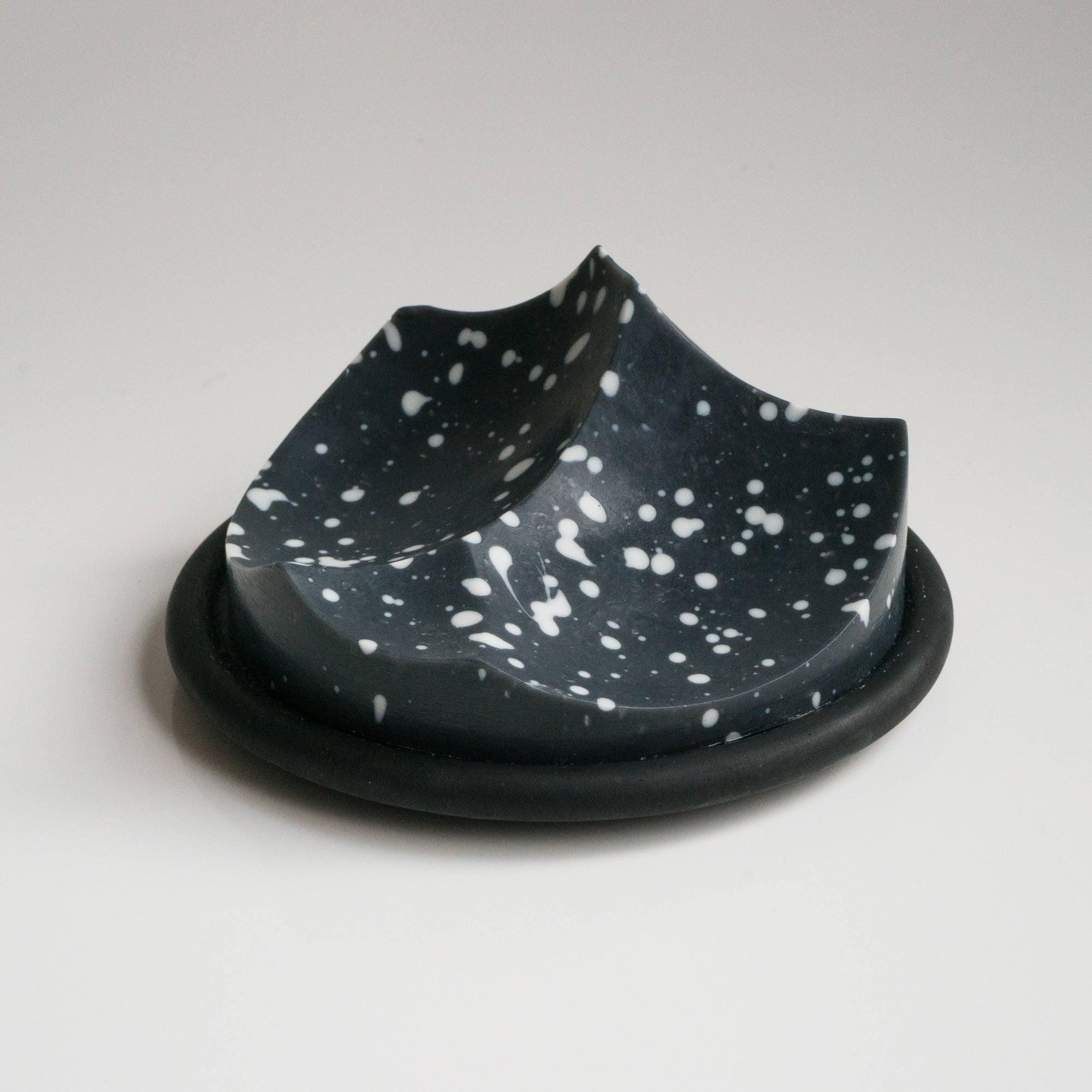 A uniquely shaped bar of soap with a black base and speckled with white dots, resting on a black surface.