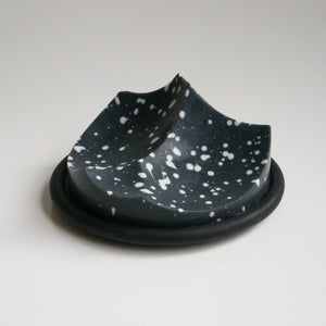 A uniquely shaped bar of soap with a black base and speckled with white dots, resting on a black surface.