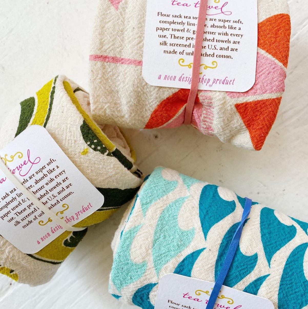 Set of folded tea towels with colorful patterns and tags on a white surface