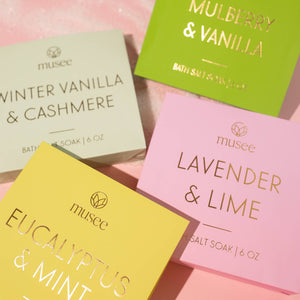 Four bath salt boxes with different scents on a pink background