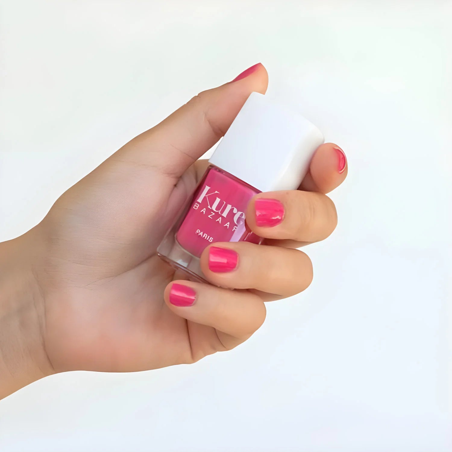 Hand holding a pink nail polish bottle with a white cap on a light background