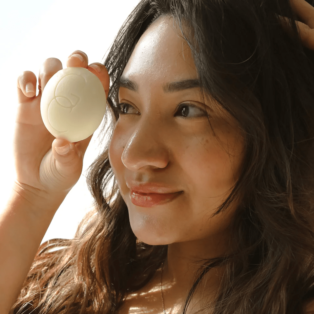 A woman holding a Good Condition organic lotion bar to her face.