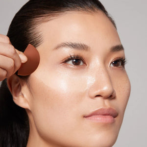 Woman applying cream to her face with an applicator.