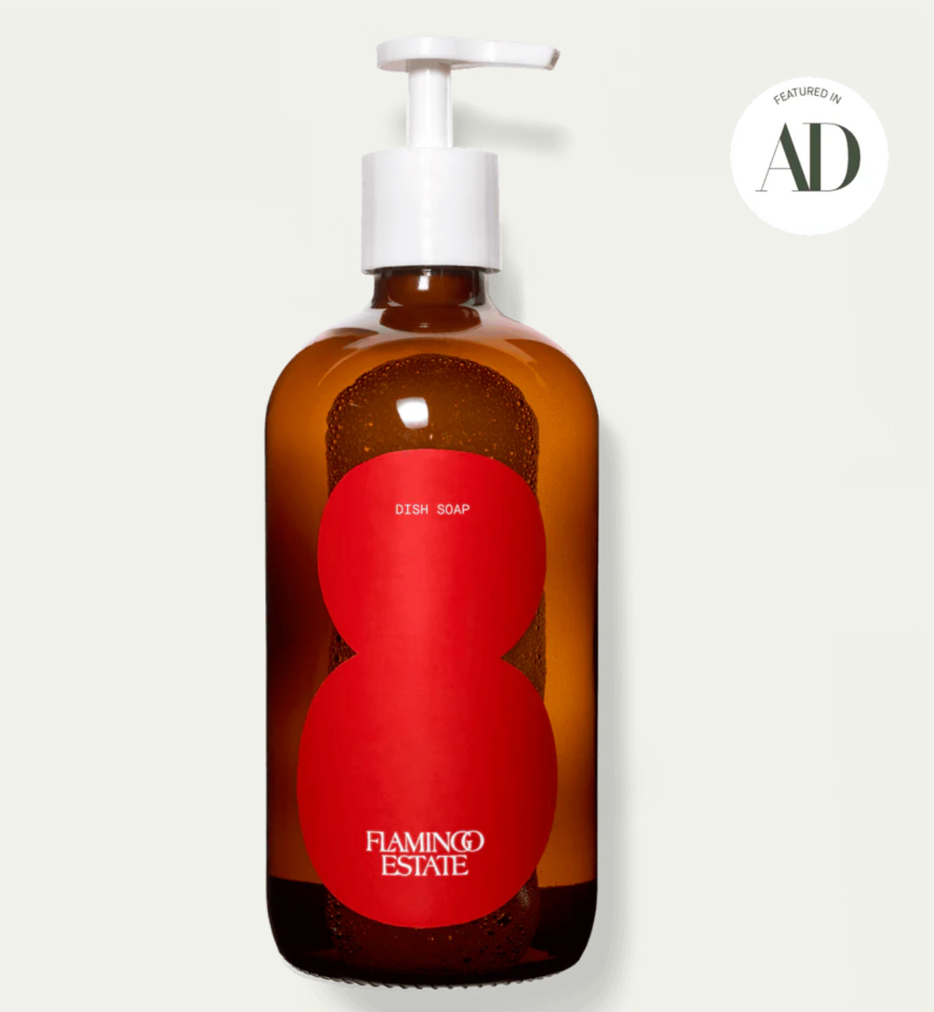 A clear pump bottle with a label that has 'Flamingo Estate' written on it and a large red tomato design behind it. There is a white cap on the bottle.