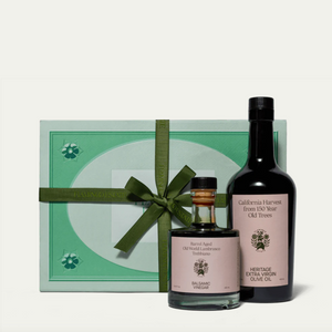 A gift set containing a bottle of olive oil and a smaller bottle of balsamic vinegar, packaged in a box tied with a green ribbon.