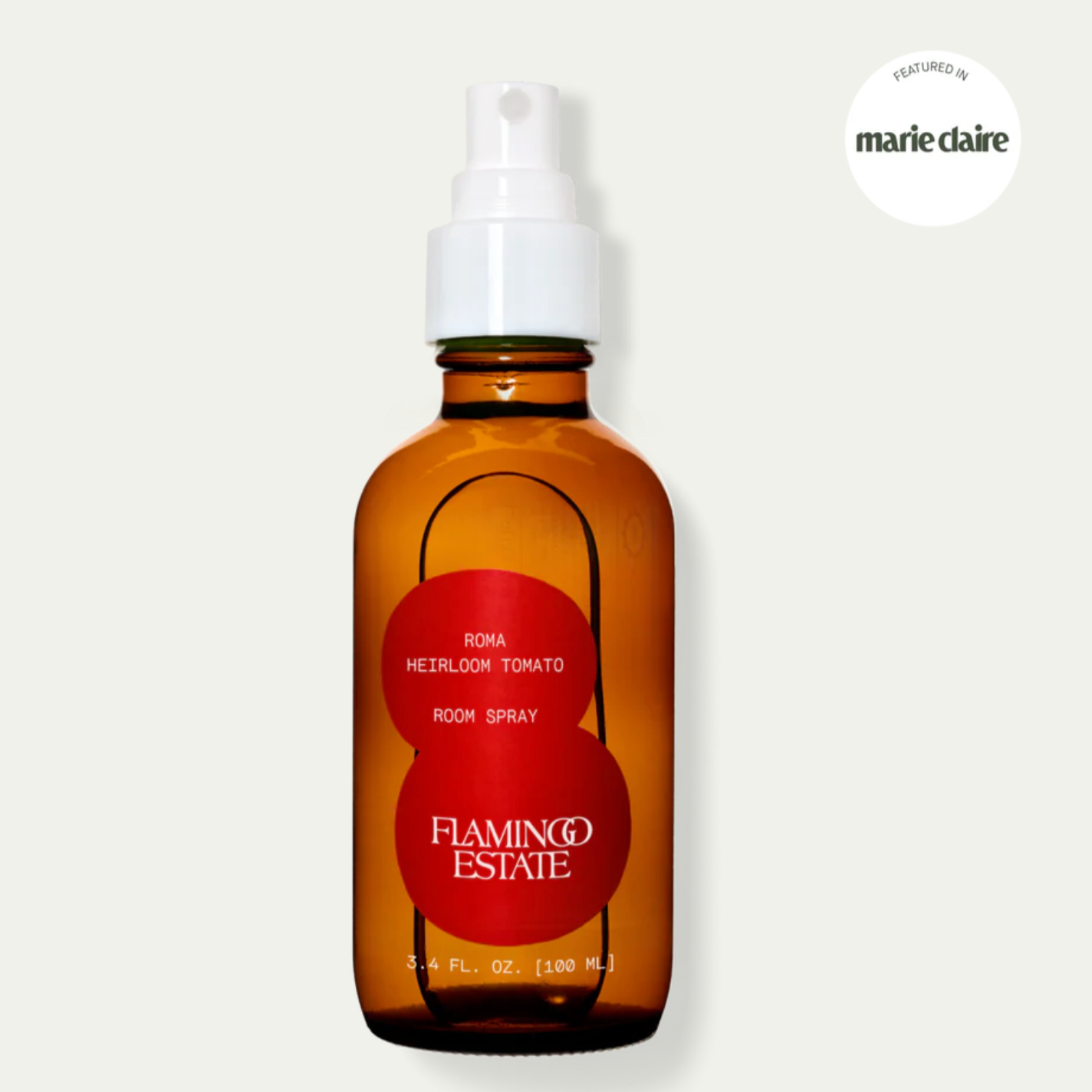 A brown amber glass bottle with a white spray nozzle, labeled 'Flamingo Estate Room Spray, Roma Heirloom Tomato'. The label is red and white with the product name and the brand logo visible.