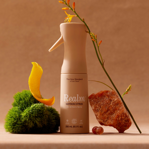 Beige spray bottle labeled 'Realm' with natural elements on a brown background