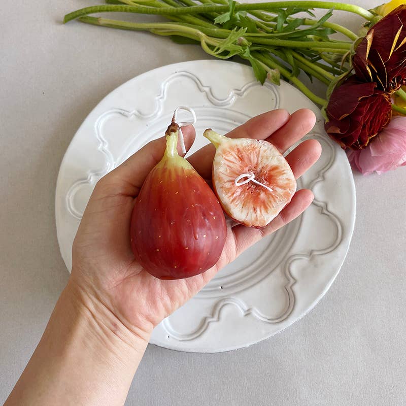 A person holding two fig shaped candles above a saucer. 