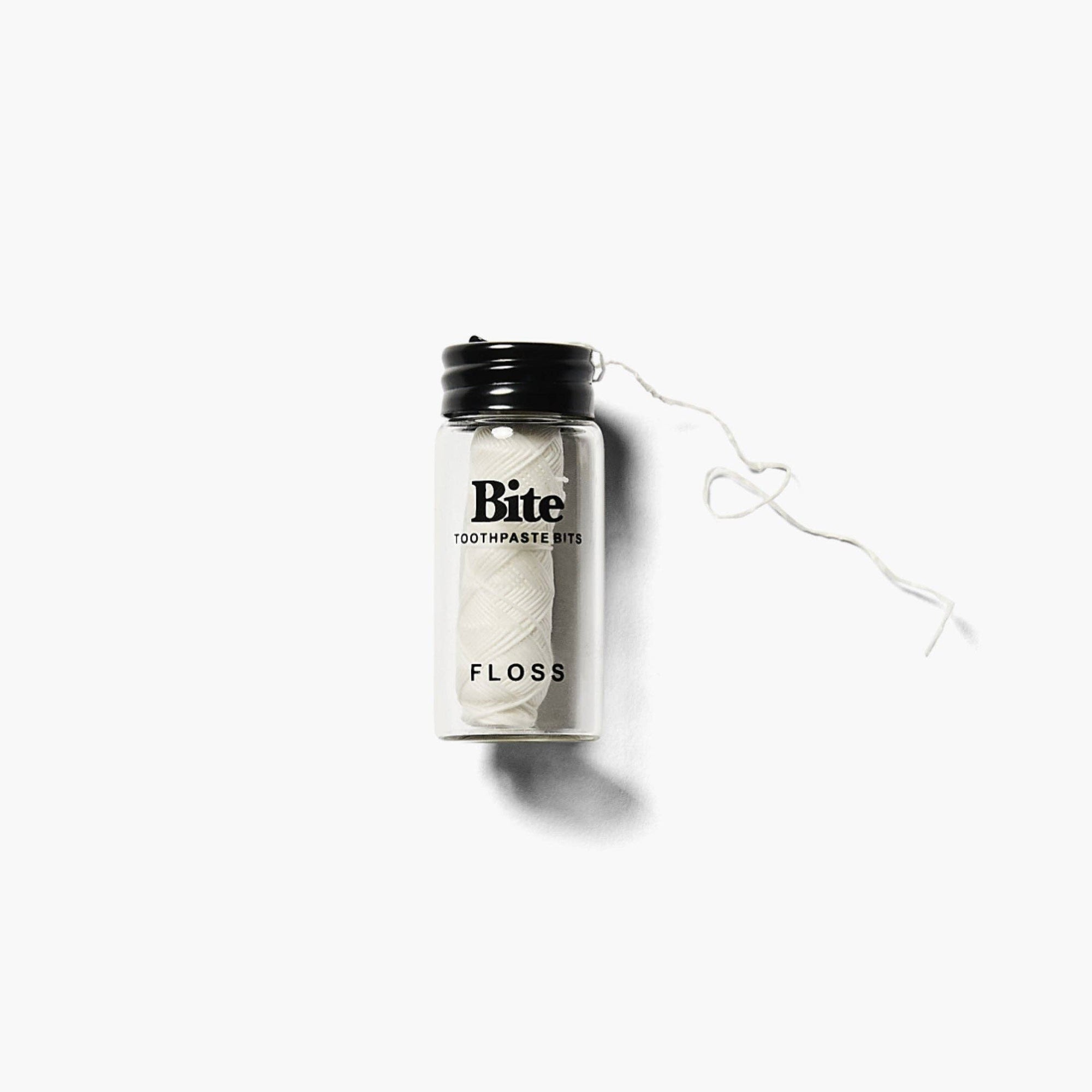 A glass bottle labeled 'bite eco-friendly floss' with a piece of dental floss tied to it, placed on a white background.