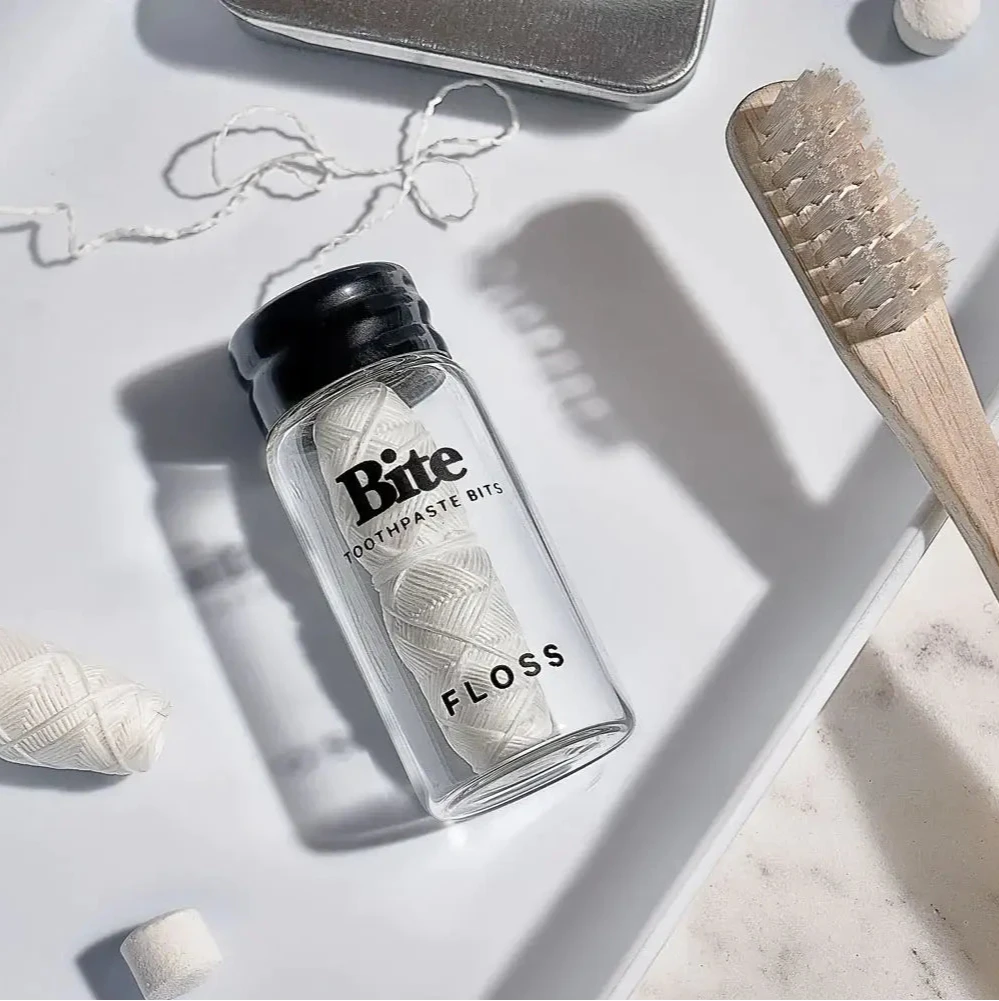A glass bottle labeled 'bite eco-friendly floss' with a piece of dental floss tied to it, placed on a white background.