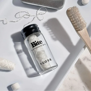 A white surface with a toothbrush, floss, a toothpaste bit and a travel case. 