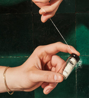 A person pulling floss from a glass container in front of a green tile wall. 