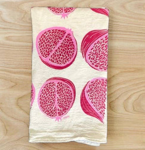 A folded beige cotton tea towel with a silkscreened pomegranate design in red.