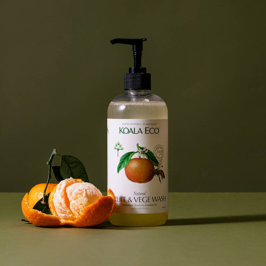 A bottle of koala eco fruit and veggie cleaner and an orange on a green background. 