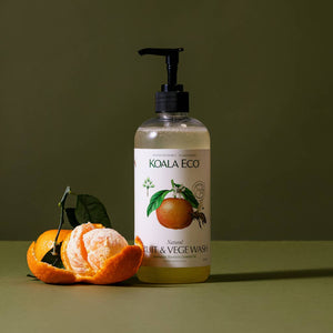 A bottle of koala eco fruit and veggie cleaner and an orange on a green background. 