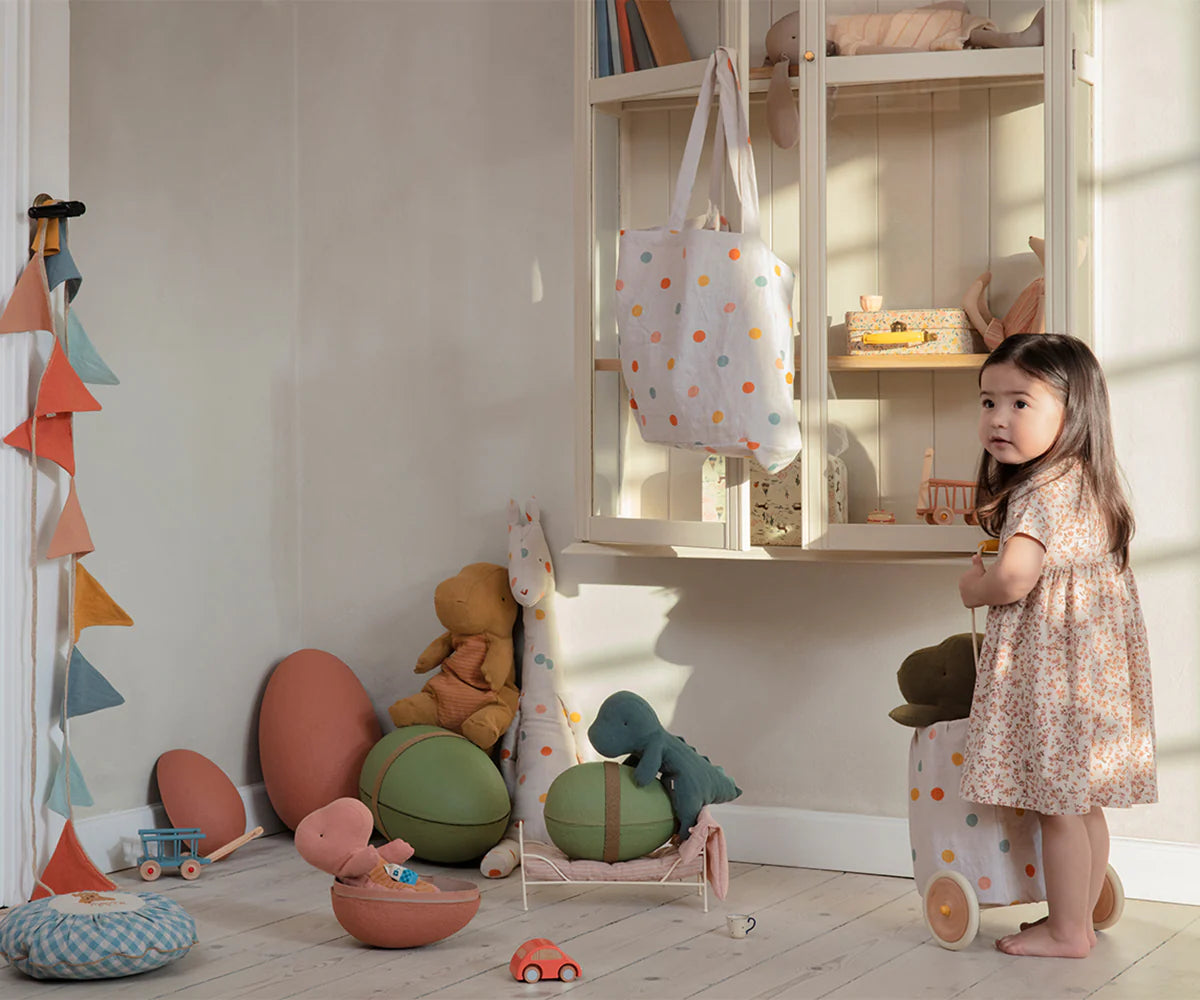 Child standing in a playroom with toys and a shelf.