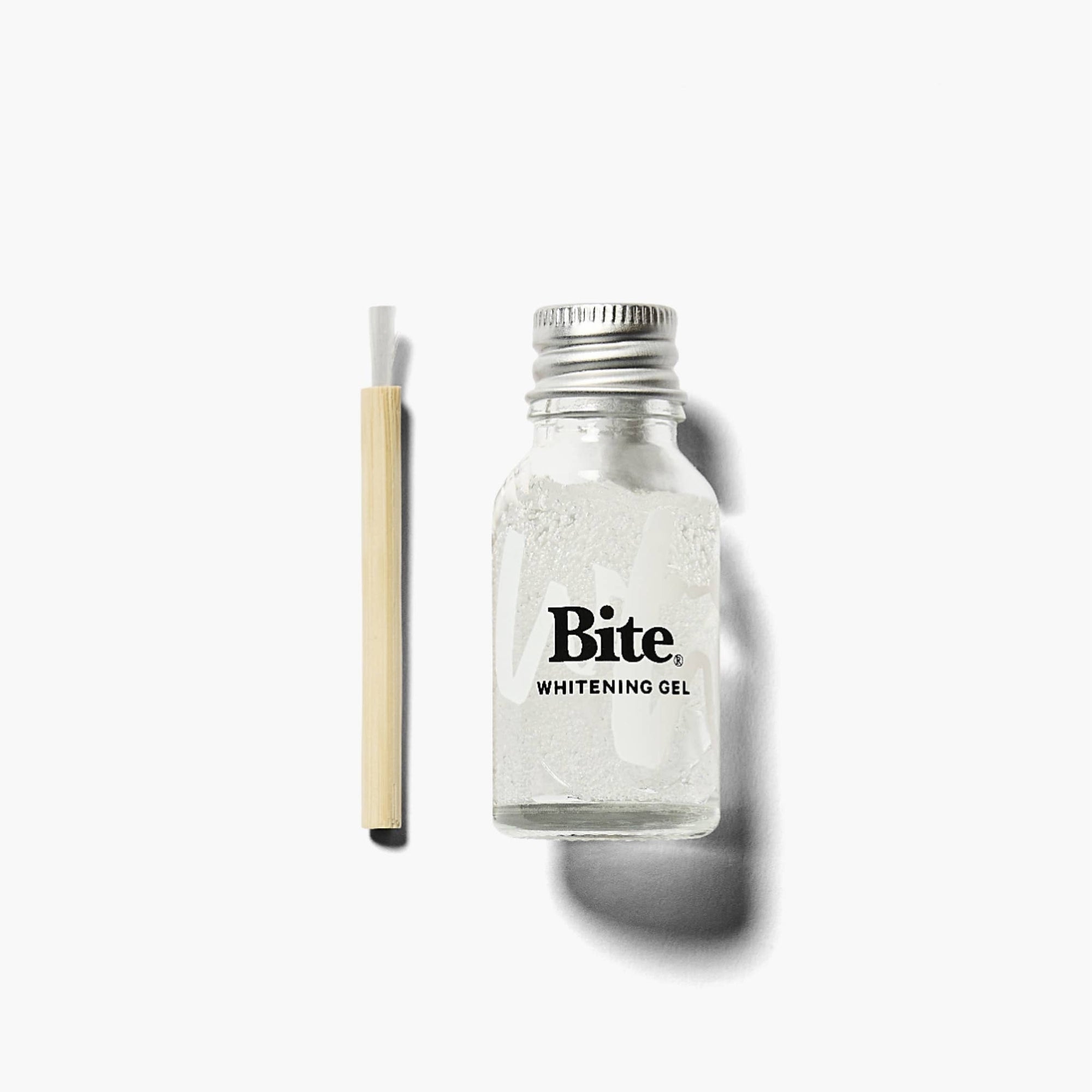 A bottle of Bite Tooth Whitening Gel, next to a bamboo applicator.