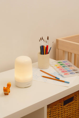 A Vitruvi Glow diffuser on a desk with pencils and art supplies