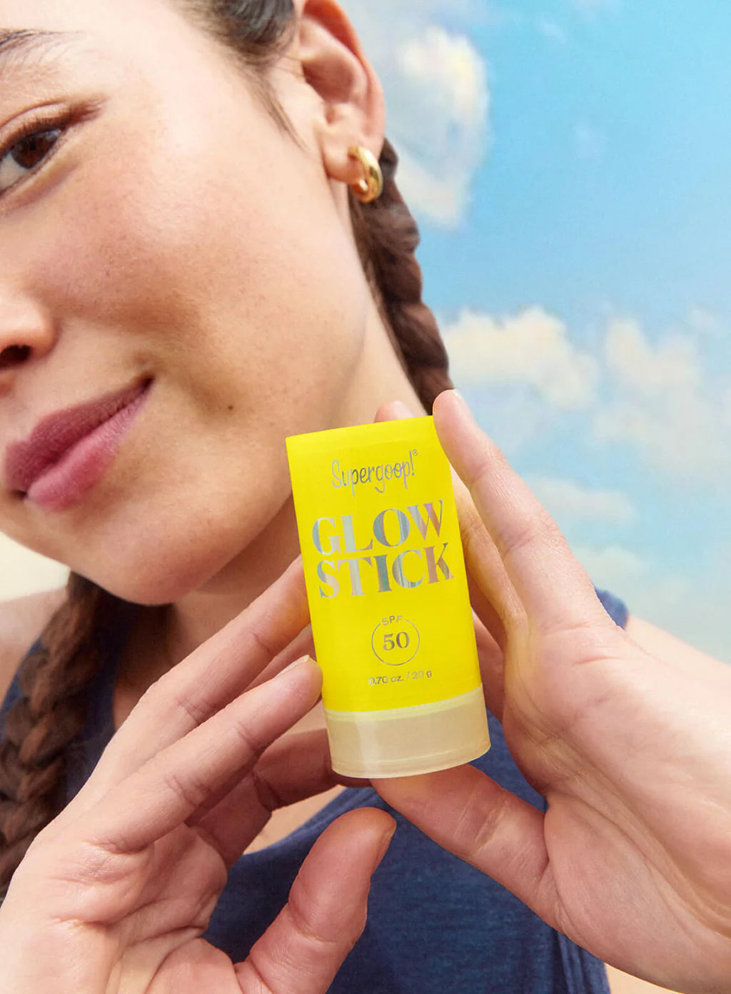 Person holding a yellow 'Glow Stick' sunscreen stick with a blue sky background