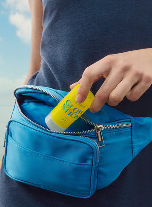 Person placing a yellow bottle labeled 'Glow Stick' into a blue bag with a blue sky background.