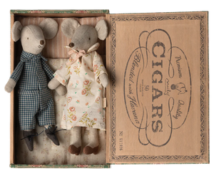 A set of two mouse figures, one in a blue checkered outfit and the other in a floral dress, placed inside an open cigar box with a brown interior.