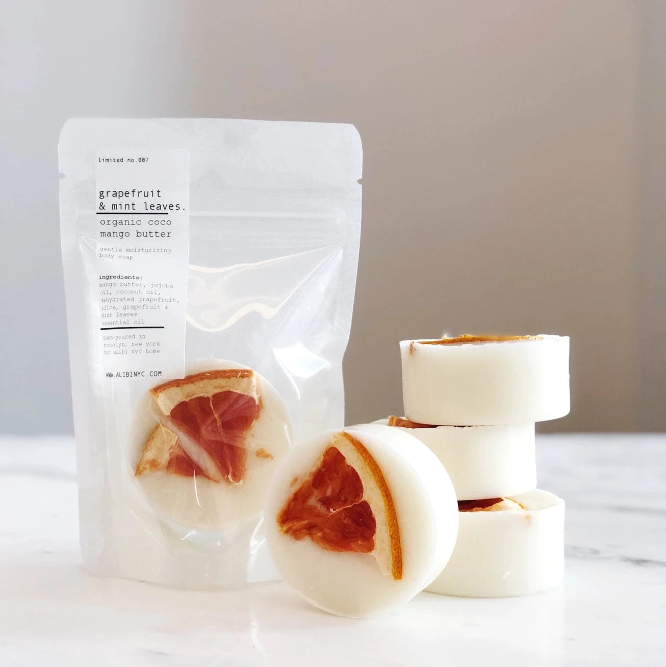 A stack of lavender grapefruit soaps on a marble surface, next to a rice paper ba with a soap inside. 