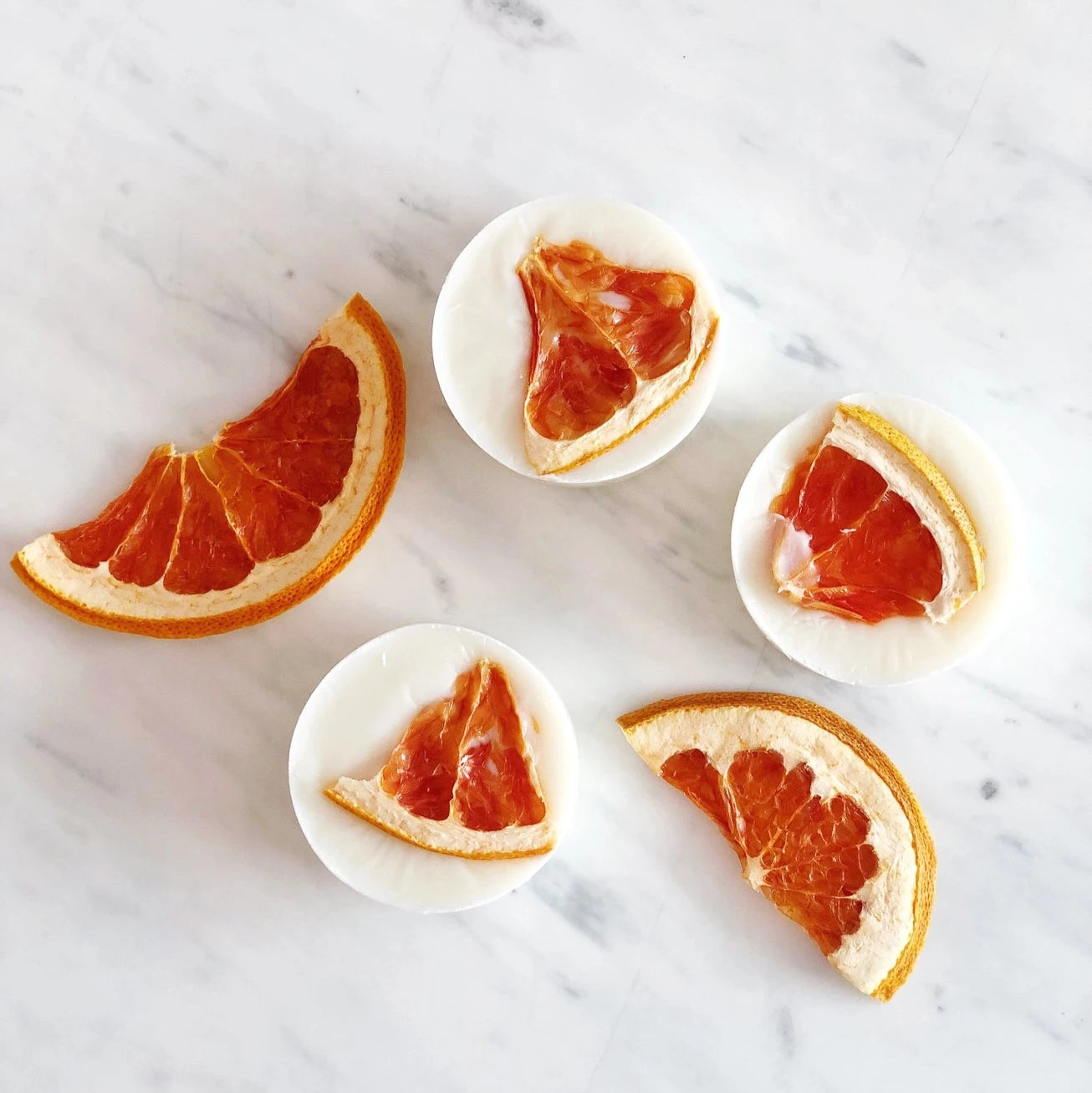 A stack of lavender grapefruit soaps on a marble surface, next to a rice paper ba with a soap inside. 
