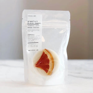 White packaging of grapefruit and mint leaves soap on a white surface with a blurred background