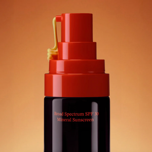 Black sunscreen bottle with red cap on a warm brown background