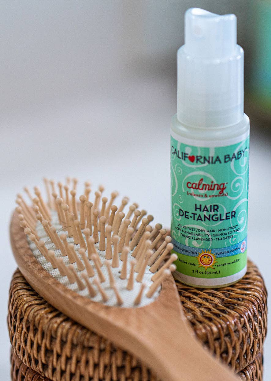 California Baby hair de-tangler bottle with a wooden brush on a textured surface